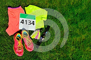 Running shoes, marathon race bib number, runners gear and energy gels on grass background, sport, fitness