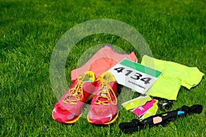 Running shoes, marathon race bib number, runners gear and energy gels on grass background, sport, fitness and healthy lifestyle