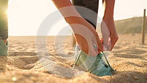 Running shoes - woman tying shoe laces on sandy beach at sunset