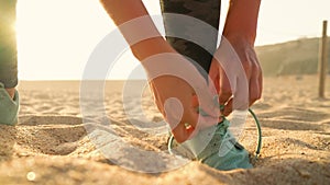 Running shoes - woman tying shoe laces on sandy beach at sunset. Slow motion
