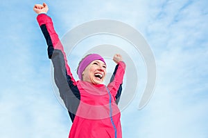 Running and sport success. Happy woman celebrating victory and raises his hands up. Female runner successful against the blue sky