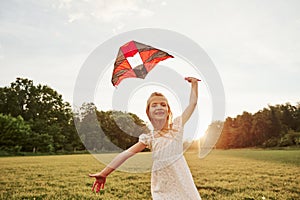 Running to the camera. Happy girl in white clothes have fun with kite in the field. Beautiful nature
