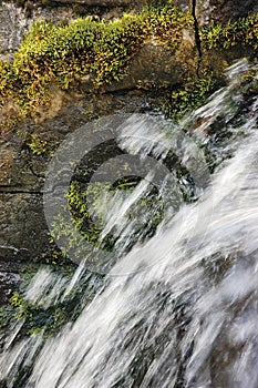 Running water cascade waterfall streaming splashes, decorative granite stonewall background, green moss, grey rock stone wall