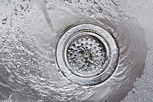 Running water flowing going down drain in stainless steel kitchen sink