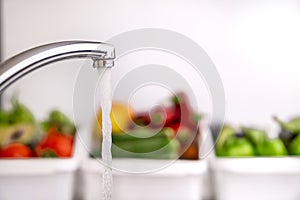 Running water from the tap in the kitchen and fruits and vegetables in the background