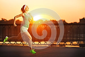 Running woman. Runner is jogging in sunny bright light on sunrise. Female fitness model training outside in the city on a quay.