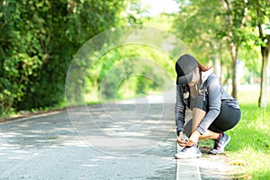 Running woman tying laces of running shoes before jogging through the road in the workout nature park.