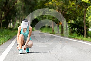 Running woman tying laces of running shoes before jogging through the road in the workout nature park.