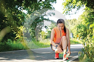 Running woman tying laces of running shoes before jogging through the road in the workout nature park.