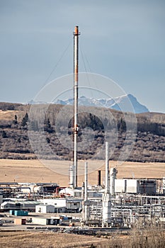 Rural Alberta gas plant with flare stack and industrial equipment portrait view overlooking hillside and mountain near Cochrane