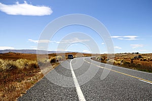 Rural asphalt road winding through a picturesque landscape of rolling mountains in New Zealand.