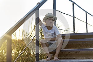 Rural boy in straw hat sitting outdoors at wooden stairs