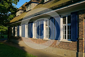 Rural brick wall building with white sash windows with stained glass and blue shutter panels at dusk.