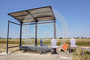 A rural bus stop next to fields and old chair damage