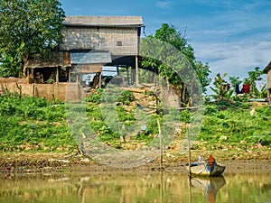 A rural Cambodian house on stilts next to a riverbank.