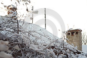 Rural chimneys and antennas on a snow-covered roof and tree branches