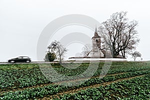 Vidiecka krajina s rozmazaným pohybom auta a gotickým kostolom v obci Ludrová na Slovensku