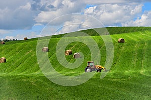 Rural country landscape with alfalfa field and cereal hay bales and tractor with fork loader in summer season