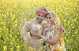 Rural couple holding Indian rupee notes in agriculture field