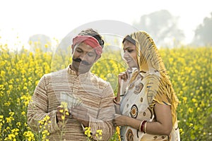 Rural couple holding Indian rupee notes in agriculture field