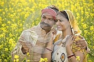 Rural couple holding Indian rupee notes in agriculture field