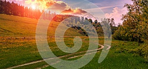 Rural dirt road at sunset. Green grass field and mountain landscape