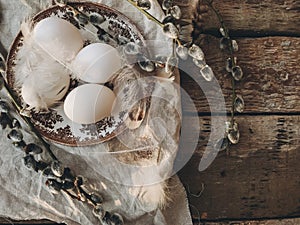 Rural Easter still life. Natural eggs, vintage plate, feathers, pussy willow on rustic table