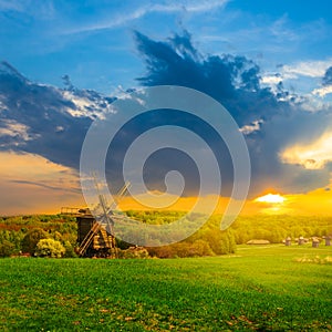 Rural ethnic landscape, green fields with wooden windmill at the  sunset