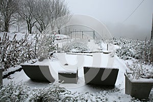 The rural garden in winter clothes. Garden furniture covered with snow in cloudy winter day.