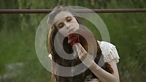 Rural girl in white dresses look at the rooster in her hands