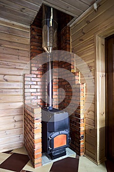 Rural home interior element. Cast iron steel wood stove burning warm on floor tile inside brick fireplace, with carbon