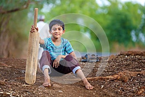 Rural Indian Child sitting on ground with bat