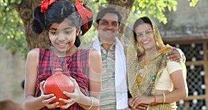 Rural Indian family with surprised daughter holding piggy bank