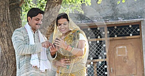 Rural Indian wife looking at her husband texting on mobile phone at village