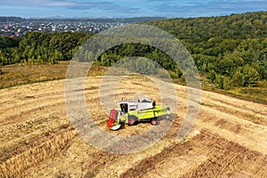 Rural landscape. Grain harvester at the border of a wheat field with the forest. In the distance the village. Shot from a drone.