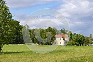 Rural landscape with green field, yellow countryside house in the middle and beautiful white clouds in the blue sky