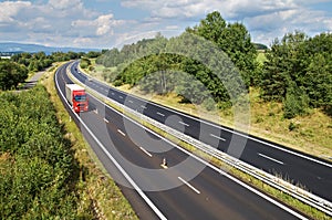 The rural landscape with a highway lined with trees, red truck and cars on the road