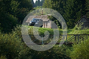 Rural landscape, a lonely homestead in the forest - a log cabin, a bathhouse and an SUV on the edge of a ravine with a bridge