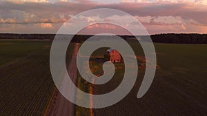Rural landscape with old abandoned barn and a dirt road at sunset. Aerial view