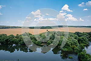 Rural landscape with a river and trees reflecting in its waters and growing on its banks. Agricultural field in the background the