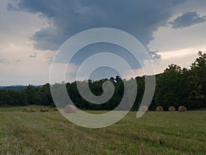 Rural landscape with rolls of hay, meadow and roll bales during overcast stormy summer day