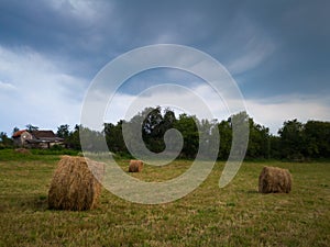 Rural landscape with rolls of hay, meadow and roll bales during overcast stormy summer day