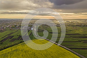 Rural landscape on spring or summer day. Aerial view of green, plowed and blooming fields, house roofs and a road on sunny dawn.