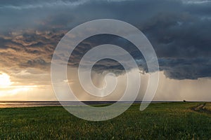 Rural landscape. Storm clouds over the lake at sunset. Green fields and meadows. Golden sunset