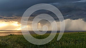 Rural landscape. Storm clouds over the lake at sunset. Green fields and meadows. Golden sunset