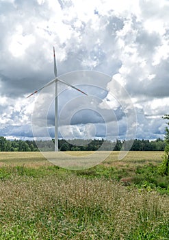 Rural landscape with wind turbine, windmill for electric power production - closeup, sky with stormy clouds in the background.