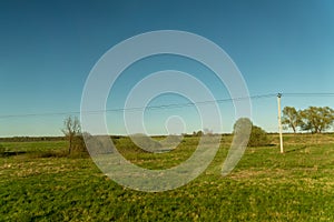 Rural llate spring landscape. Green field and power line along the road. Russian Country side