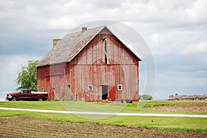 A rural old, red barn with a red pickup truck.