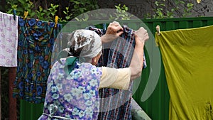 Rural old woman hanging laundry on clothespins outdoor