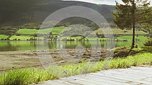 A rural panorama beach view of green farmland, trees, quiet lake and mountains in the countryside, nature summer scenery with sun
